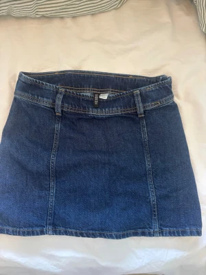 Mörkblå jeanskjol från H&M - En fin och söt mörkblå jeanskjol från H&M. Kjolen har en rakpassform och är normallängd.