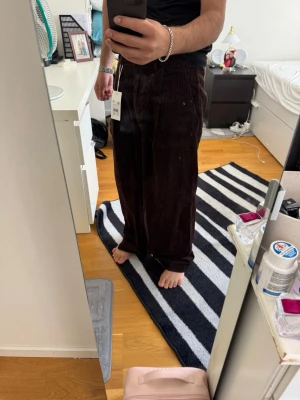 Bruna vida manchesterbyxor - Säljer ett par mörkbruna manchesterbyxor med breda ben och hög midja. Byxorna har klassiska räfflor och en avslappnad passform som ger en cool och trendig look. Perfekta för dig som vill ha en retrovibe i garderoben.
