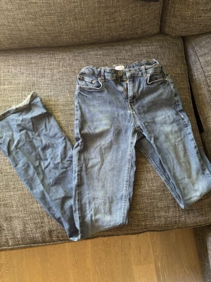 Blåajeans bootcut/flare - Säljer ett par ljusblå jeans med resår i midjan. Jeansen har klassiska fem fickor och knappgylf. . Märket är Grunt köpta från kidsbrandstore