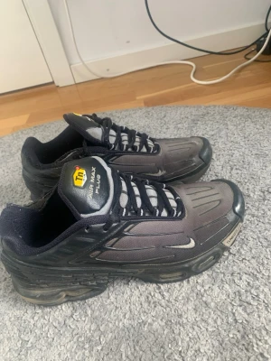 Nike Air Max Plus svarta sneakers - Nike Air Max Plus sneakers i svart med vita detaljer och Tn-logga på plösen. Skorna har en sportig design med synlig Air-sula och meshmaterial på ovandelen. Klassiska snörningar och diskret Swoosh på sidan. Perfekta för dig som gillar streetwear.