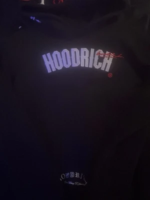 Svart hoodie från Hoodrich - Säljer en svart hoodie från Hoodrich med stor vit logga på bröstet och en mindre logga nedtill. Klassisk passform med huva och magficka. Perfekt för dig som gillar streetwear och vill ha en stilren men ändå tydlig look.