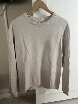 Beige stickad tröja från Zara - Snygg beige stickad tröja från Zara med rund halsringning och ribbade muddar vid ärmslut och nederkant. Tröjan har en enkel och stilren design som passar perfekt till många olika outfits. Tillverkad i mjukt material för extra komfort.
