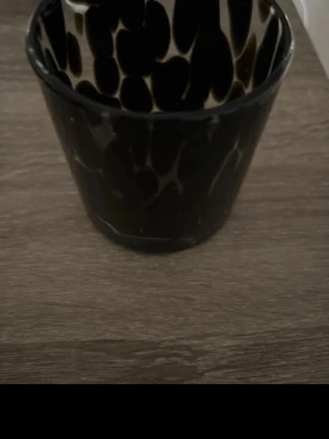 Svart kruka med mönster - Säljer en svart kruka i keramik med unikt prickigt mönster i beige och svart. Perfekt som inredningsdetalj för växter eller förvaring. Krukan har en rund form och en glansig yta som ger ett modernt intryck.