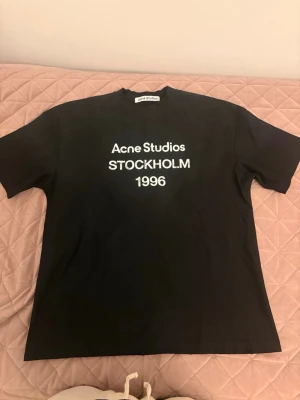 Svart Acne Studios t-shirt  - Svart t-shirt från Acne Studios med vit text 'Acne Studios STOCKHOLM 1996' på bröstet. Klassisk passform med rund hals och korta ärmar. Perfekt basic-plagg för en clean och stilren look. Dm för mer bilder, pris kan diskuteras 
