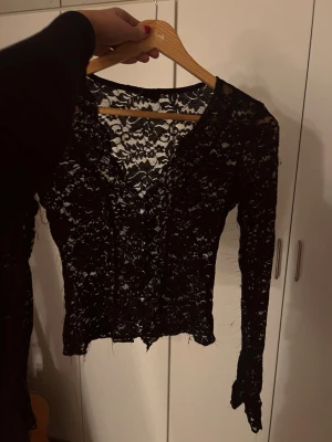 Svart spetsblus med v-ringning - Säljer en svart långärmad blus från Gina Tricot i genombruten spets med v-ringning. Toppen är i XS, är figurnära och har knappar 🦋 Det är tyvärr som lösa trådar från spetsen, se bild 3 🖤 