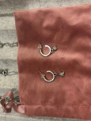Silvriga örhängen med stjärna och strass - Säljer ett par silvriga örhängen i form av halvmånar dekorerade med små gnistrande stenar och en liten stjärna upptill. Örhängena har push back-lås och ger en glittrig och trendig look. Perfekta för dig som gillar detaljer och stjärntema.