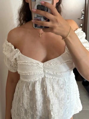 Vit offshoulder topp med volang - Supersöt vit offshoulder topp med volangdetaljer och struktur i tyget. Toppen har puffiga korta ärmar och en romantisk v-ringning. Perfekt för sommarens alla tillfällen och ger en riktigt trendig vibe.