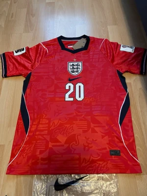 England röd matchtröja nr 20 - Snygg röd England fotbollströja från Nike med nummer 20 och namnet Palmer på ryggen. Tröjan har svarta och vita detaljer, broderat landslagsemblem på bröstet och klassisk sportig passform. Perfekt för dig som älskar fotboll och vill stötta England.