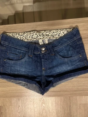 Mörkblå denimshorts med låg midja - Ett par blå lågmidjade shorts från Mango Jeans. Bra skick men finns tecken på användning. Midjemått: 36 cm tvärs över. Pris kan diskuteras! 