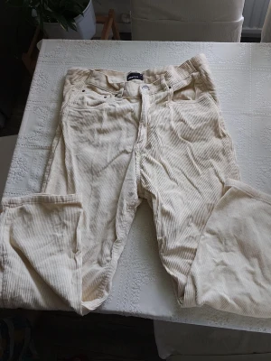Vida beige manchesterbyxor Gina Tricot - Säljer ett par ljusbeige manchesterbyxor från Gina Tricot i storlek 36. Byxorna har vida ben, klassisk femficksmodell och stängs med knapp och dragkedja. Tillverkade i mjuk manchester med tydlig struktur. Perfekta för en trendig och avslappnad look.