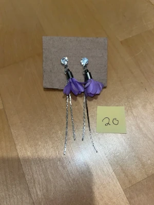 Korvakorut - Pari kertaa käytetyt korvakorut. Liilat kukat ja roikkuvat hopeiset nauhat. Desinfioitu ja puhdistettu käytön jälkeen. Koukkujen materiaali ei tiedossa. Eläintalous MMM Katsothan myös muut ilmoitukseni Tarjoa 