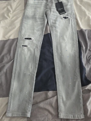 Ljusgrå slitna skinny jeans - Säljer ett par ljusgrå skinny jeans med slitningar och färgstänk. Materialet är klassisk denim och passformen är smal. Perfekta för dig som gillar en trendig och avslappnad stil. !Obs! det ska vara storlek 30 men de är produkt fel så de är strlk 28 typ!!!