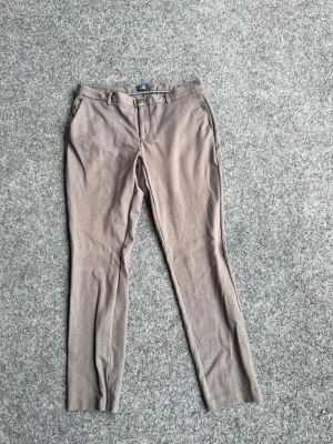 Beige kostymbyxa med smal passform - Snygga beige kostymbyxor med smal passform och klassisk design. Byxorna har bälteshällor, sidofickor fram och två bakfickor med knapp. Perfekta för en stilren look och passar till skjorta eller kavaj.
