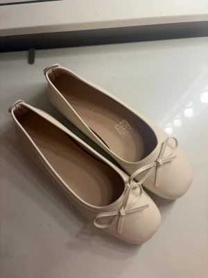 Vita ballerinaskor med rosett - Säljer ett par stilrena vita ballerinaskor med rund tå och söt rosettdetalj framtill. Skorna har en klassisk design och är tillverkade i ett slätt material som ger en clean look. Perfekta att matcha med jeans eller klänning för en enkel och snygg stil. Helt oanvända o säljer då de ej passar 💕