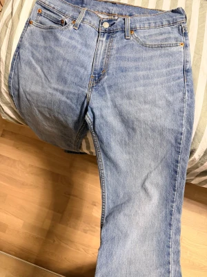 Ljusblå raka jeans levis - Klassiska ljusblå jeans med rak passform och fem fickor. Jeansen har normal midja, bälteshällor och stängs med knapp och dragkedja. Tillverkade i denim med snygga kontrastsömmar och kopparfärgade nitar. Perfekta för en avslappnad stil. L: 31 W: 32