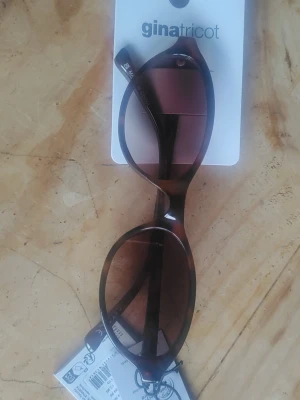 Bruna ovala solglasögon Gina Tricot - Snygga solglasögon från Gina Tricot med oval form och bruna bågar i sköldpaddsmönster. Glasen är tonade i brunt och ger en cool retrovibe. Perfekta för att lyfta din stil under soliga dagar.