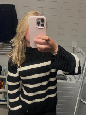 Svartvit randig stickad tröja - Säljer en svart stickad tröja med breda vita horisontella ränder. Tröjan har en högre rund halsringning och långa ärmar med lite lösare passform. Perfekt för dig som gillar en klassisk men trendig look.
