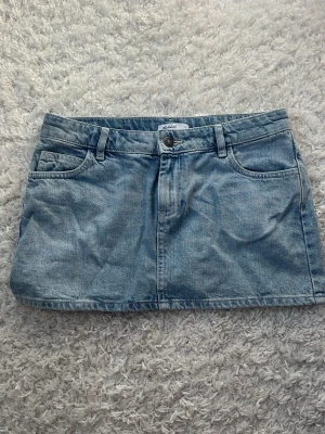 Ljusblå jeanskjol  - Trendig ljusblå jeanskjol från subdued. Kjolen har två snygga bakfickor med lock och knappdetalj. Perfekt att matcha med en enkel topp för en cool look. Edanst använd ett fåtal gånger.