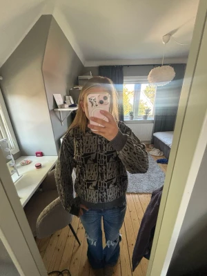 Grå stickad tröja med grafiskt mönster - Säljer en grå stickad tröja med svart grafiskt mönster. Tröjan har rund hals, ribbade muddar och avslut. Oversized passform som ger en avslappnad look. Perfekt att matcha med jeans för en cool vardagsstil. Vintage och går inte att köpa i någon butik.