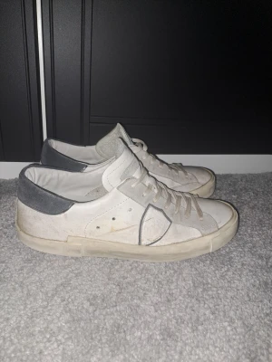 Vita och grå låga sneakers - Snygga vita sneakers med grå detaljer och lågt skaft. Skorna har vita snören, grå hälkappa och en beige sula. Materialet ser ut att vara en mix av läder och mocka. Perfekta för en clean och avslappnad stil. Box medföljer