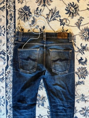 Nudie jeans premium  - Säljer ett par Nudie Jeans Co denimjeans i en klassisk mörkblå tvätt. Tillverkade av premiumdenim med den karaktäristiska Nudie-blekningen som ser ännu bättre ut med tiden. Jeansens är slimfit på storlek det är inte skinny. Fast pris 