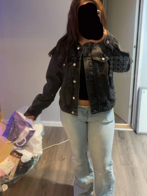 Svart jeansjacka med silverknappar - Snygg svart jeansjacka i klassisk modell med raka linjer och silverfärgade knappar. Jackan har två bröstfickor med lock och knapp samt en avslappnad passform. Perfekt att slänga över en t-shirt för en cool look.