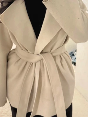 Beige kappa med knytskärp från Nelly - Stilren beige kappa från Nelly med breda slag och knytskärp i midjan. Kappan har en rak passform och är tillverkad i ett mjukt tyg som ger en lyxig känsla. Perfekt för att lyfta din outfit under kyliga dagar.