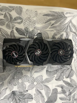 MSI Rtx 2080 8gb - Säljer ett svart grafikkort från MSI med tre stora fläktar och robust kylsystem. Kortet har en modern design med detaljer i rött och silver, perfekt för gaming eller tunga datoruppgifter. Byggt i metall och plast för bästa prestanda.