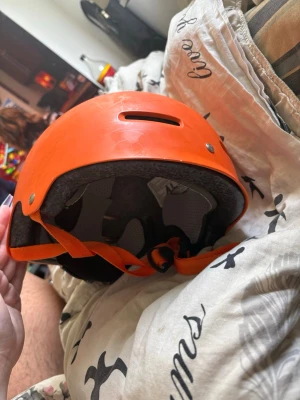 Orange sporthjälm med ventilationshål - Snygg orange hjälm med justerbart hakband och ventilationshål upptill. Hjälmen har en klassisk rund form och är tillverkad i hårdplast med mjuk vaddering på insidan för extra komfort. Perfekt för skate, cykel eller andra sportaktiviteter.