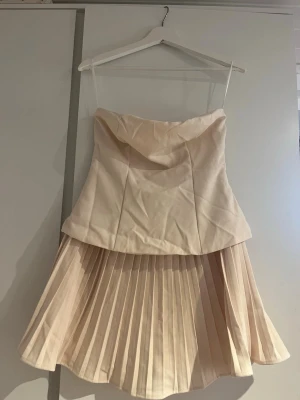 Champagnefärgad axelbandslös klänning - Snygg axelbandslös klänning i champagnefärg med.Perfekt för dig som vill sticka ut med en elegant och modern look. Ny och oanvänd!!
