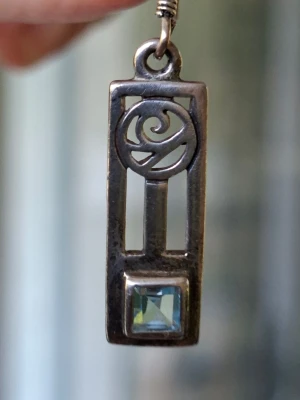 Silver, Sterling 925, örhängen från Kit Heath Jewellery, England - Retroörhängen i Sterlingsilver med slipad topas i himmelsblått. Designen är inspirerad av Art nouveauarkitekten Charles Rennie Mackintosh's ornamentik från 1900-talets början.    Plattans längd är 22 mm och bredden 18 mm. Örhängets totala längd är ca 40 mm. Örhängena är köpta i England kring 1990-talet och har aldrig använts. Mycket gott skick! Originalasken medföljer.                             