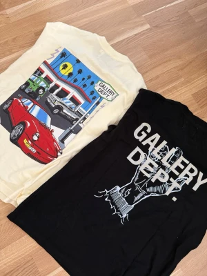 2 st Gallery Dept t-shirts med tryck - Två t-shirts från Gallery Dept. En svart med stort 'BURIED ALIVE!' tryck och grafiskt motiv på ryggen, samt en ljusgul med bensinmack- och bilmotiv på ryggen och liten logga fram. Båda har rund hals och korta ärmar. Perfekta för dig som gillar streetwear och coola prints.