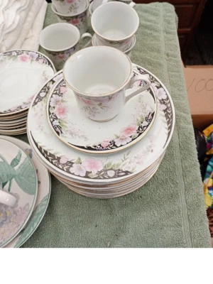 Kaffeservis med blommönster - Säljer en klassisk kaffeservis i porslin med vackert blommönster i rosa, vitt och grönt samt guldkant. Setet innehåller koppar, fat och assietter med matchande design. Perfekt för fika eller samlingar.