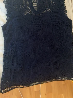 Svart spetslinne med detaljer - Säljer ett svart ärmlöst linne med vackra spetsdetaljer och broderat mönster. Toppen har en rundad halsringning 