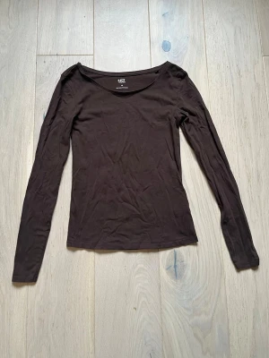 Brun långärmad topp från Lager 157 - Mörkbrun långärmad topp från Lager 157 i mjuk bomullsblandning (95% bomull, 5% elastan). Enkel och tight passform, perfekt att styla lager på lager eller till jeans. 