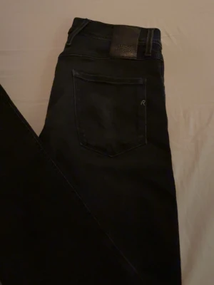 Svarta slim fit jeans från Replay - Snygga svarta jeans från Replay i slim fit-modell. Jeansen har klassisk femficksdesign, svarta sömmar och en läderpatch med logga bak i midjan. Materialet är stretchigt för extra komfort och passform.