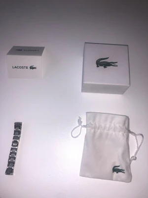 Nytt Lacoste armband  - Stilrent armband i silverfärgad metall från Lacoste med länkdesign och ingraverade krokodilmönster på länkarna. Levereras med original ask och tygpåse med Lacoste-logga. Perfekt accessoar för dig som gillar klassisk och sportig stil. Fraktar från 1-2 dagar efter köp. Priset kan diskuteras 