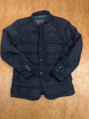 Massimo Dutti Jacka - Stilren mörkblå pufferjacka med knäppning framtill och quiltad design. Jackan har ståkrage, knappdetaljer vid ärmsluten och två sidofickor. Pertekt tor kalla dagar och ger en clean look. Fodrad insida för extra varme.