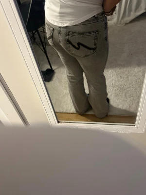 Gråa bootcut jeans från Wrangler - Säljer ett par gråa bootcut jeans från Wrangler med ikonisk W-söm på bakfickorna. Jeansen har låg midja och raka ben med lätt utsvängning. passar folk som är 150cm och är i storlek 36