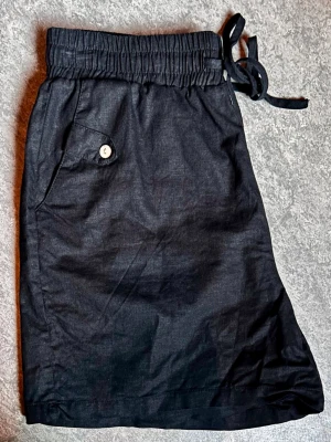 Soyaconcept svarta linneshorts (Stl M) - Svala svarta sommarshorts från Soyaconcept i stl M! Gjorda i mjuk linnemix (55% linne, 45% viskos) som skrynklar mindre. Bred resårmidja, dragsko & sidofickor med fina knappar. Perfekt luftigt skick! Mått mätt plant: Midja: ca 36cm Lårvidd: ca 33cm Längd: ca 41cm.                                               Se sista bilderna för tyglappar!