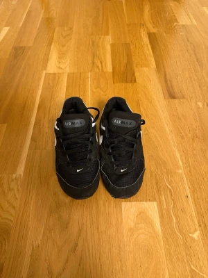 Nike Air Max svarta sneakers - Snygga svarta Nike Air Max sneakers med vita detaljer och klassisk logga på sidan och sulan. Skorna har en låg silhuett och är tillverkade i en mix av mesh och syntetmaterial för en sportig look. Perfekta för dig som gillar streetwear och vill ha bekväma skor till vardags.