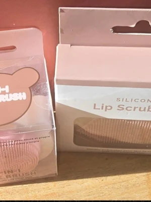 Läpp skrubb & ansiktsborste ( silikon) - Söt 2-i-1 borste i silikon för ansikte och läppar. Borsten är rosa och har små mjuka piggar som hjälper till att rengöra och exfoliera huden. Perfekt för dig som vill ha len och fräsch hy. Kommer i en praktisk förpackning med björnöron-design.