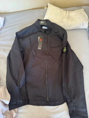 Stone Island Jacket - Säljer en svart Stone Island tun jacka då den är jättestor på mig. Den är i storlek L och är oanvänd. Jättebra nu inför sommaren när det små regnar eller blåser på kvällarna. Priset kan diskuteras!!
