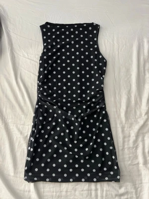 Svart prickig ärmlös klänning från SHEIN  - Snygg svart klänning med vita prickar och ärmlös design. Kort modell med rund halsringning och figurnära passform. Perfekt för dig som gillar retrovibbar och vill sticka ut lite extra.