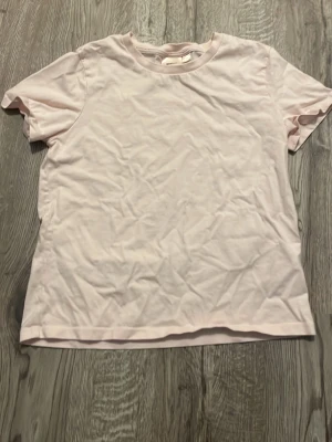 Ljusrosa basic t-shirt i bomull - Enkel och stilren ljusrosa t-shirt med rund halsringning och korta ärmar. Tillverkad i mjuk bomull, perfekt för en avslappnad och clean look. Passar till det mesta och är ett måste i garderoben.