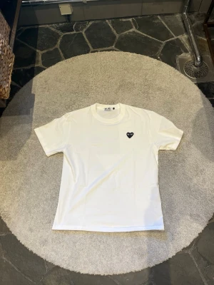 Vit Comme des Garçons PLAY t-shirt - Vit t-shirt från Comme des Garçons PLAY med det ikoniska svarta hjärte-logotypen på bröstet. Klassisk passform med rund hals och korta ärmar. Tillverkad i mjuk bomull för en skön känsla.