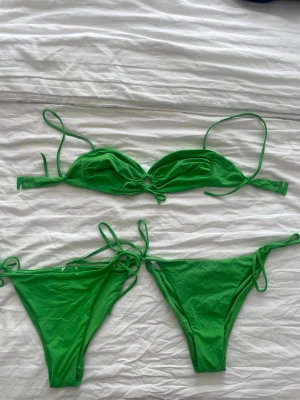 Grön bikini med knyt - Snygg grön bikini med knyt i både överdel och underdel. Överdelen har tunna axelband och en liten ringdetalj framtill. 