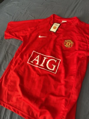 Manchester United Ronaldo tröja - Säljer en röd Manchester United matchtröja med Ronaldo och nummer 7 på ryggen. Tröjan har klubbmärke, Nike-logga och AIG som sponsor på framsidan. Tillverkad i lätt och ventilerande material, perfekt för fotbollsträning eller som supporterplagg.