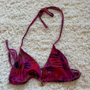 Röd-lila mönstrad bikini - Snygg trekantsbikini i rosa och lila toner. Överdelen har knyt i nacken och baktill, och underdelen har hög midja. Materialet känns mjukt och stretchigt, perfekt för stranden.