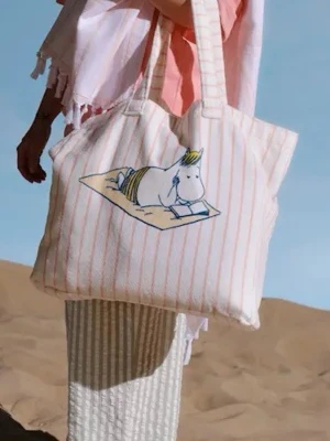 Randig shoppingväska med Muminmotiv strandväska ny - Säljer en stor tygväska med ljusrosa ränder och ett tryck av snorkfröken som ligger och läser på en filt. Väskan har breda axelband och är perfekt för att bära med sig allt man behöver. Materialet är mjukt tyg, 100% bomull. Superfin och unik design för dig som gillar Mumin!